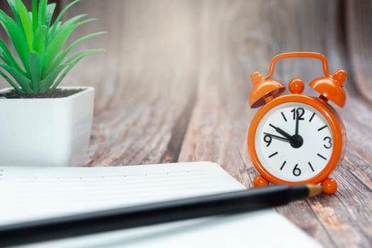 Notepad with potted plant and alarm clock set at 10 o'clock against wooden background. Business concept. Copy space.