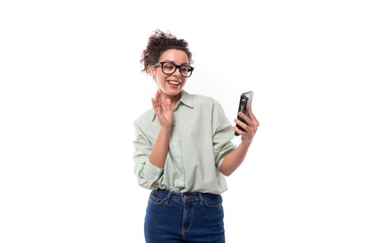 young smiling woman student with curly hair in a shirt communicates via video call on the phone.