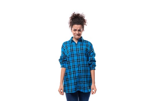 young upset curly brunette woman in a blue plaid shirt on a white background.