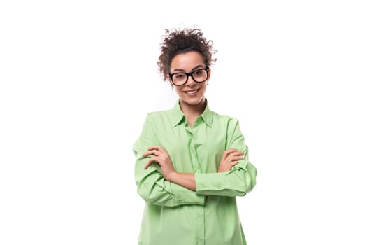 pretty young brunette curly woman in glasses is dressed in a green shirt on a white background with copy space.