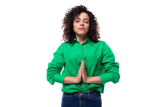 a young woman with black curly hair dressed in a green blouse is meditating.