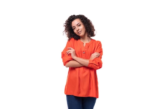 young curly brunette lady dressed in a stylish bright orange blouse on a white background with copy space.