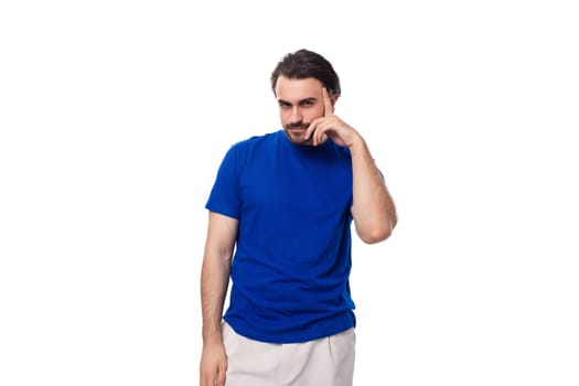 young attractive brunette man with a beard in a blue t-shirt with a mockup on a white background with copy space.