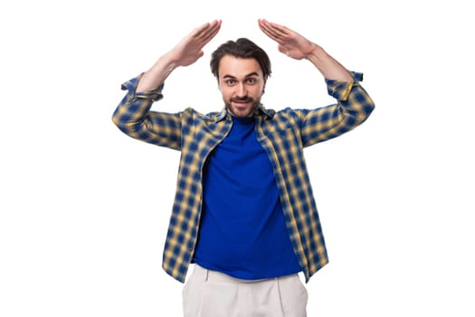 charming well-groomed brunette macho man with a beard and mustache in a blue shirt on a white background with copy space.