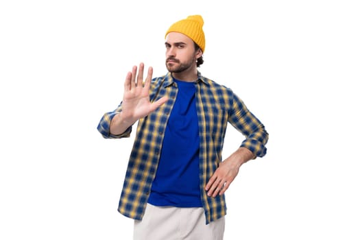 well-groomed authentic young european brunette man with a brutal beard and mustache dressed in a yellow hat and blue shirt.