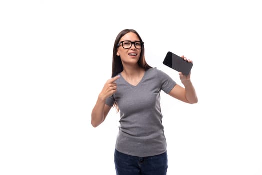 young promoter woman in glasses dressed in a gray t-shirt uses a smartphone on a white background with copy space.