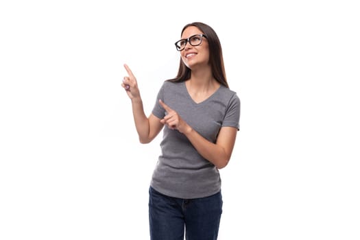 well-groomed young woman in glasses dressed in a gray t-shirt points to the space for advertising.