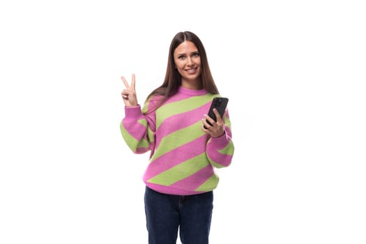 young slender caucasian woman with straight black hair dressed in a striped pink pullover communicates in social networks using a smartphone.
