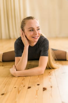 Young slim woman is doing some twine to stretch. Joyful talented woman in fitness class. Female ballerina portrait.