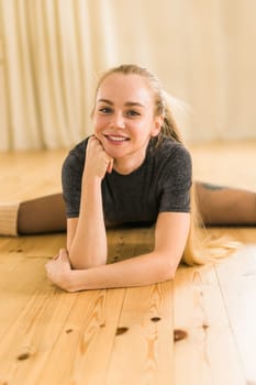 Young slim woman is doing some twine to stretch. Joyful talented woman in fitness class. Female ballerina portrait.