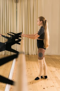 Female ballet dancer practicing at barre in dance studio - dance and ballerina