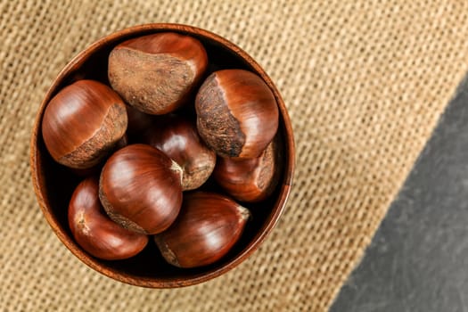 Overhead shot - chestnuts in small wooden bowl on jute tablecloth