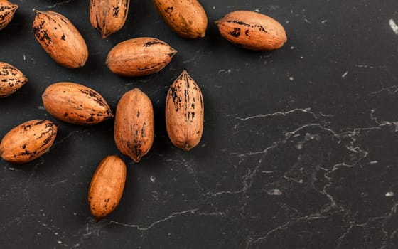 Whole pecan nuts on black marble board, flat lay photo with space for text down right