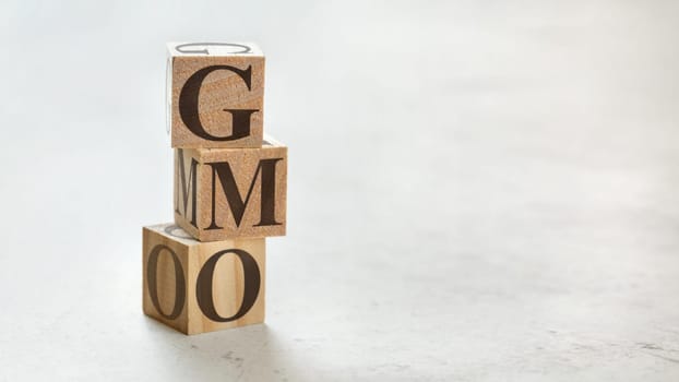 Pile with three wooden cubes - letters GMO meaning Genetically Modified Organism on them, space for more text / images at right side.