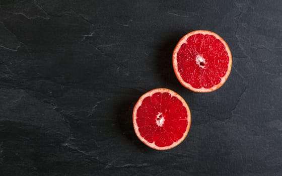 Flat lay photo - pink grapefruit cut in two halves, on black slate board