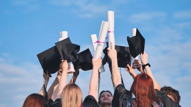 College graduates raise their hands with caps and diplomas to the sky