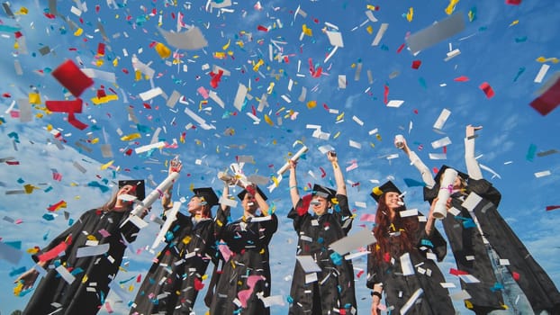 Happy graduates throw colorful confetti against a blue sky