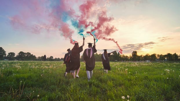 Graduates in costume walk with a smoky multi-colored smoke at sunset.