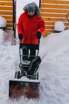 A man clear snow from backyard with snow blower. Winter season and snow blower equipment.