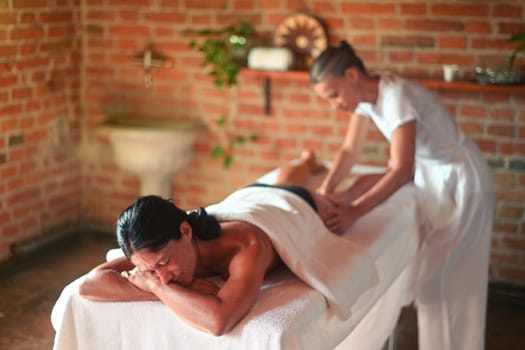 professional caucasian female physiotherapist masseuse performing leg massage to hispanic latino brunette woman in spa clinic