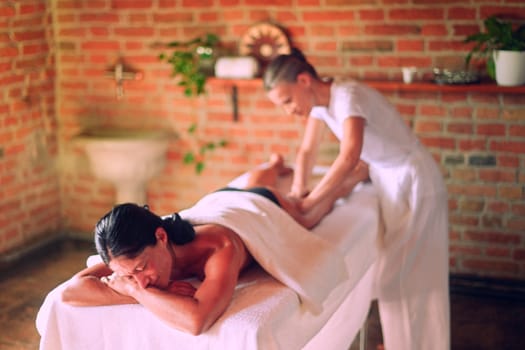 professional caucasian female physiotherapist masseuse performing leg massage to hispanic latino brunette woman in spa clinic