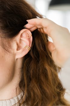 Cropped close-up shot of a young woman with two asymmetrical golden ear cuffs. Female with golden ear cuffs, side view