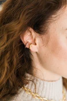 Cropped close-up shot of a young woman with two asymmetrical golden ear cuffs. Female with golden ear cuffs, side view