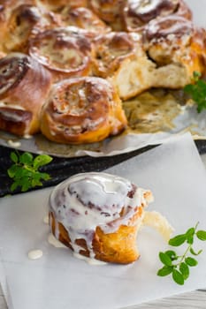 cooked baked sweet cinnabon with cream in baking paper on a wooden table.