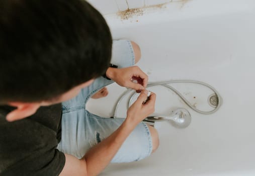One young Caucasian recognizable guy with a brunette wraps white tow on the nut from the faucet while sitting right in the bathroom at home, close-up view from above.Step by step.