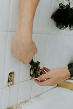 One young Caucasian unrecognizable man manually tightens the nut from the faucet with two hands with an adjustable wrench in the bathroom sticking out of the wall, standing in the bathroom, close-up side view.Step by step.