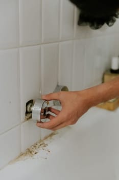 One young Caucasian unrecognizable guy manually installs a round piece from a faucet onto pipes with nuts protruding from the wall, standing bent over in the bathroom, close-up side view.Step by step.