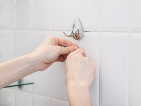 One young Caucasian man unscrews an old metal towel rack in the bathroom with a curly small screwdriver, reflected in it, close-up side view.