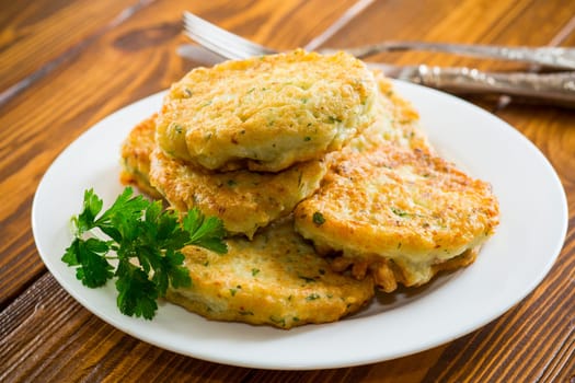 cooked fried potato cutlets with herbs, in a plate on a wooden table.
