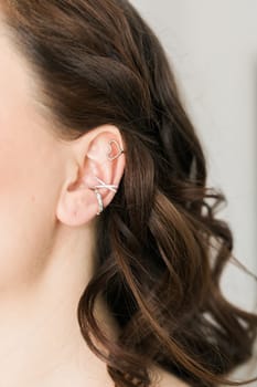 Cropped close-up shot of a young woman with asymmetrical silver ear cuffs. Female with metal ear cuffs, side view.