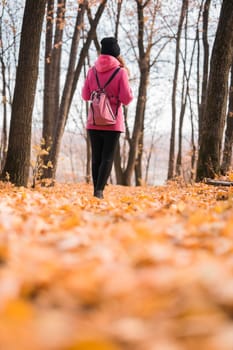 Back view of a girl walking on autumn park in fall season. Millennial generation and youth.