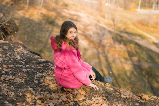 Beautiful happy smiling girl with long hair wearing black hat and pink jacket posing in autumn park. Outdoor portrait day light. Autumn mood concept. Copy empty space for text.