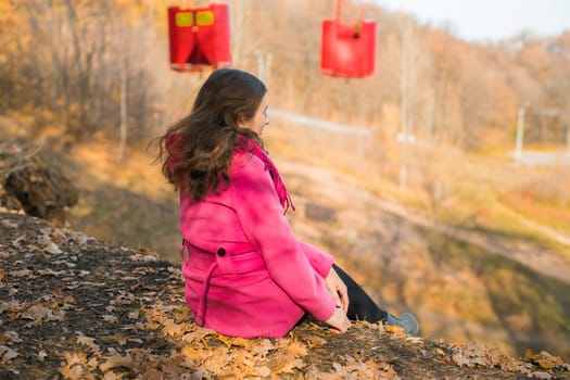 Back view of a girl woman resting on autumn park in fall season and look at the cable car. Generation Z and gen z youth. Copy empty space for text