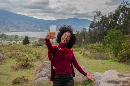 smiling and excited afro blogger girl showing her followers a lagoon in the mountains. High quality photo