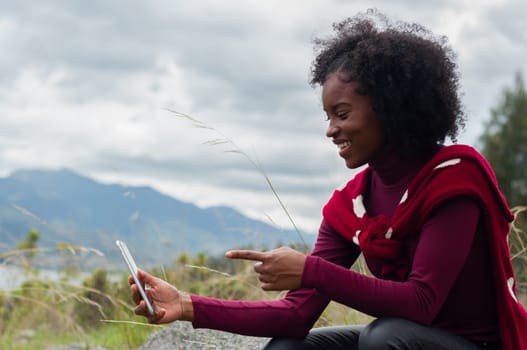 copyspace of pretty smiling afro girl interacting with her followers on a mountain. High quality photo