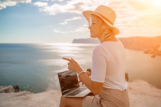 Freelance women sea working on the computer. Good looking middle aged woman typing on a laptop keyboard outdoors with a beautiful sea view. The concept of remote work