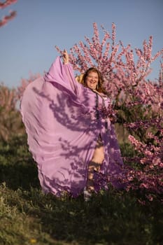 Woman blooming peach orchard. Against the backdrop of a picturesque peach orchard, a woman in a long pink dress and hat enjoys a peaceful walk in the park, surrounded by the beauty of nature