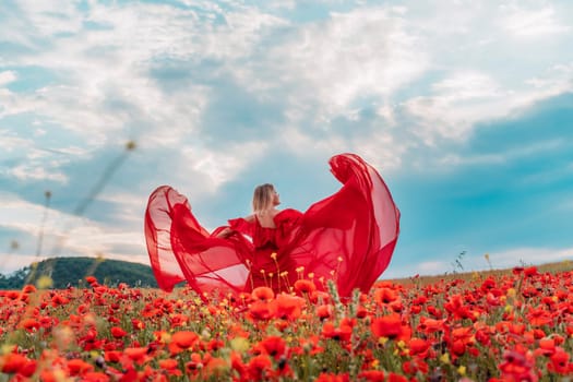 Happy woman in a long red dress in a beautiful large poppy field. Woman stands with her back in a long red dress, posing on a large field of red poppies.
