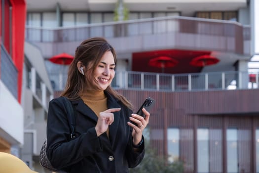 Smiling Asian businesswoman wearing a suit stands tall in the city using an application on her mobile phone. Read news on your smartphone fast connection Check outdoor mobile apps.