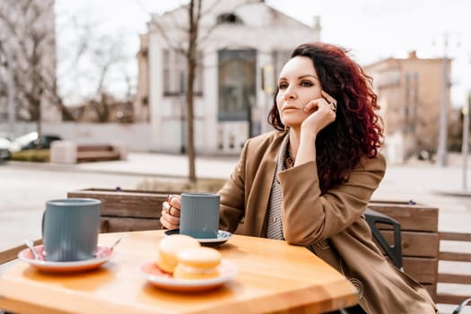 stylish woman in a beige coat drinks coffee outdoors in a cafe