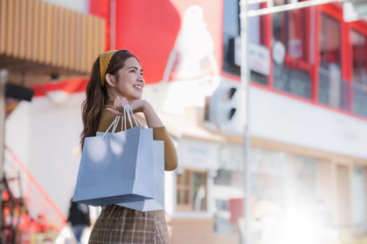 Beautiful Asian woman holding shopping bags and smiling while shopping on Black Friday outside the mall.