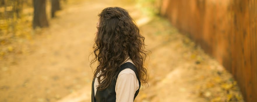 Girl in fall forest. Woman with long curly hair. Beautiful sunlight in the forest. Hair care. Millennial Generation and youth