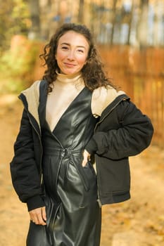 Attractive young woman walking in autumn park, happy mood and fashion style trend and curly long brown hair. Fall season and pretty female portrait. Millennial generation