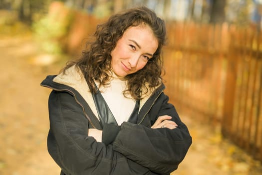 Attractive young woman walking in autumn park, happy mood and fashion style trend and curly long brown hair. Fall season and pretty female portrait. Millennial generation