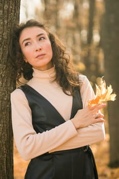 Attractive young woman walking in autumn park, happy mood and fashion style trend and curly long brown hair. Fall season and pretty female portrait. Millennial generation