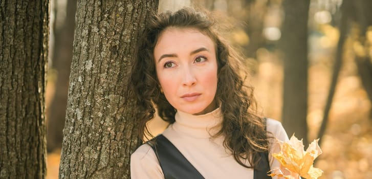 Attractive young woman walking in autumn park, happy mood and fashion style trend and curly long brown hair. Fall season and pretty female portrait. Millennial generation